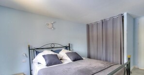 Een enkel bed met een metalen frame, een nachtkastje en een wandlamp.