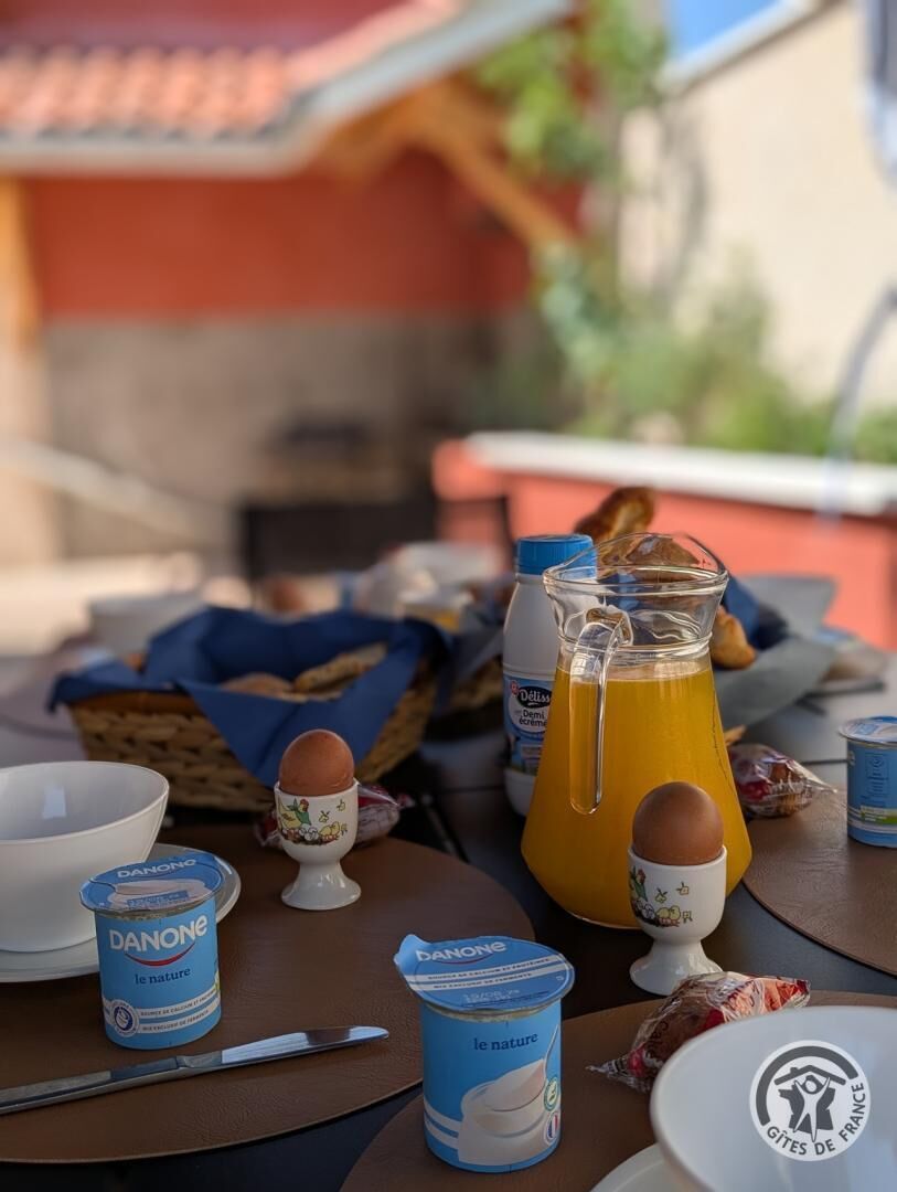 A breakfast table with a pitcher of orange juice, a bowl, a knife, and a container of Danone yogurt.