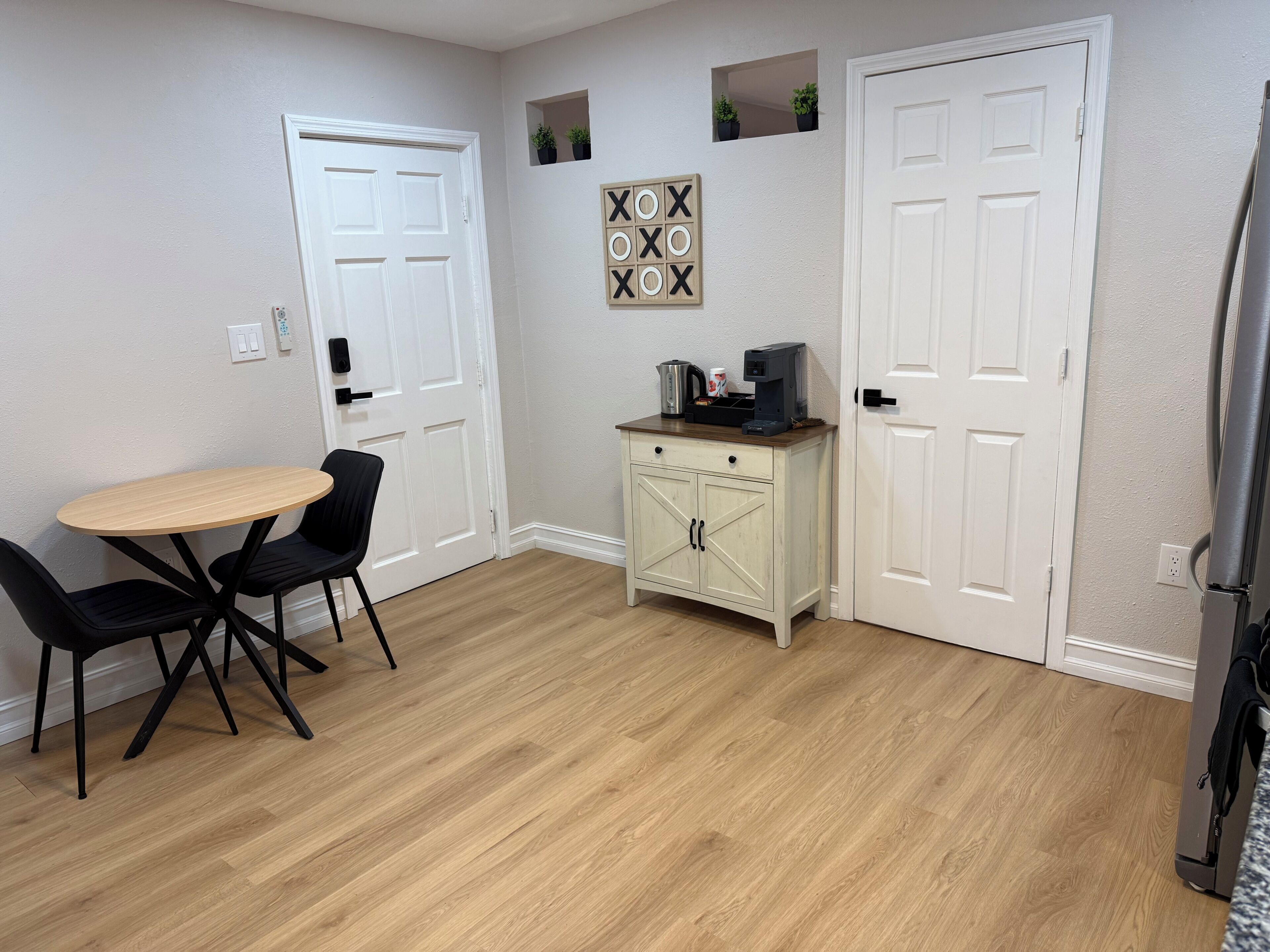 A room with a dining table, chairs, a small cabinet, and two doors.