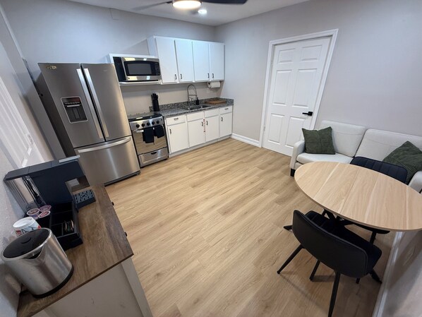 A compact kitchen with a microwave, stove, and refrigerator. There's a dining table with chairs and a white door in the background. - Modern 1BR Tampa Stay Near Downtown (Tampa)