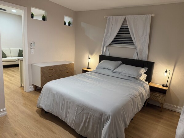Une chambre à coucher comprenant un lit, des tables de chevet, une commode, un meuble à tiroirs, un miroir et une fenêtre avec des rideaux.