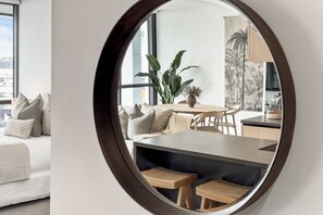 A modern interior with a round mirror reflecting a dining area, a sofa, and a large window. - Inner-City Comfort at Beaumont in Wynyard Quarter (Auckland)