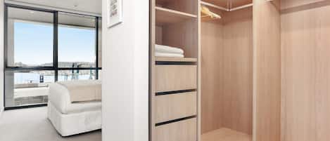 A modern bedroom with a large window, a white bed, and a walk-in closet with wooden shelving.