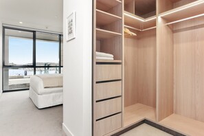 A modern bedroom with a large window, a white bed, and a walk-in closet with wooden shelving. - Inner-City Comfort at Beaumont in Wynyard Quarter (Auckland)