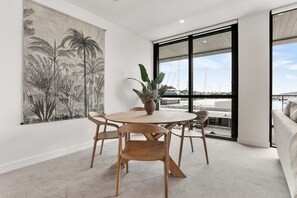 A dining area with a round table and chairs, a large plant, and a view of the marina through large windows. - Inner-City Comfort at Beaumont in Wynyard Quarter (Auckland)