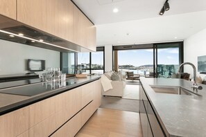A modern kitchen with a large island, a dining area with a view, and a living space with a sofa and chairs. - Inner-City Comfort at Beaumont in Wynyard Quarter (Auckland)