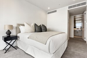 A bedroom with a bed, bedside table, lamp, and an open door leading to a bathroom. - Inner-City Comfort at Beaumont in Wynyard Quarter (Auckland)