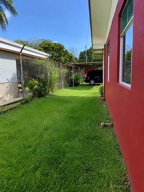 A well-maintained grassy yard with a fenced area, a covered structure, and a red building with a window.