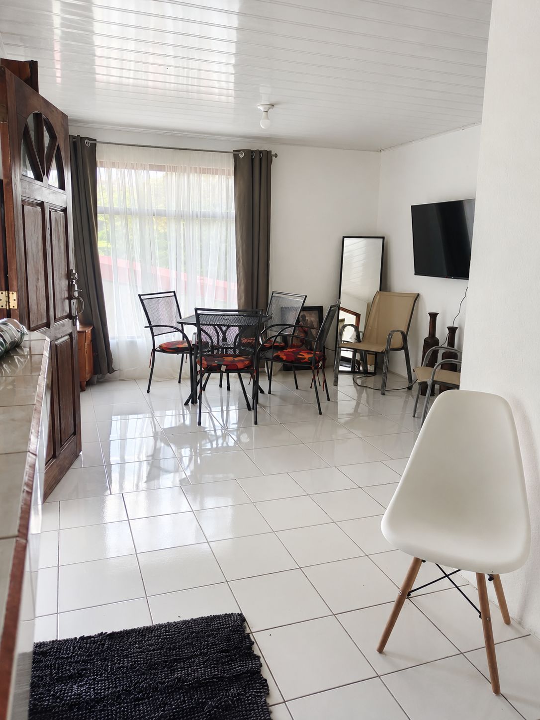 Una sala de estar moderna con comedor, un televisor de pantalla plana montado en la pared y un gran ventanal con cortinas.
