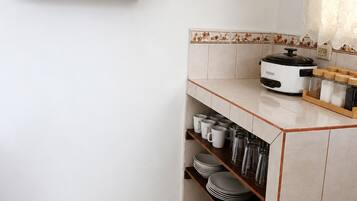 A kitchen with a built-in oven, a shelf with glassware, and a tiled backsplash.