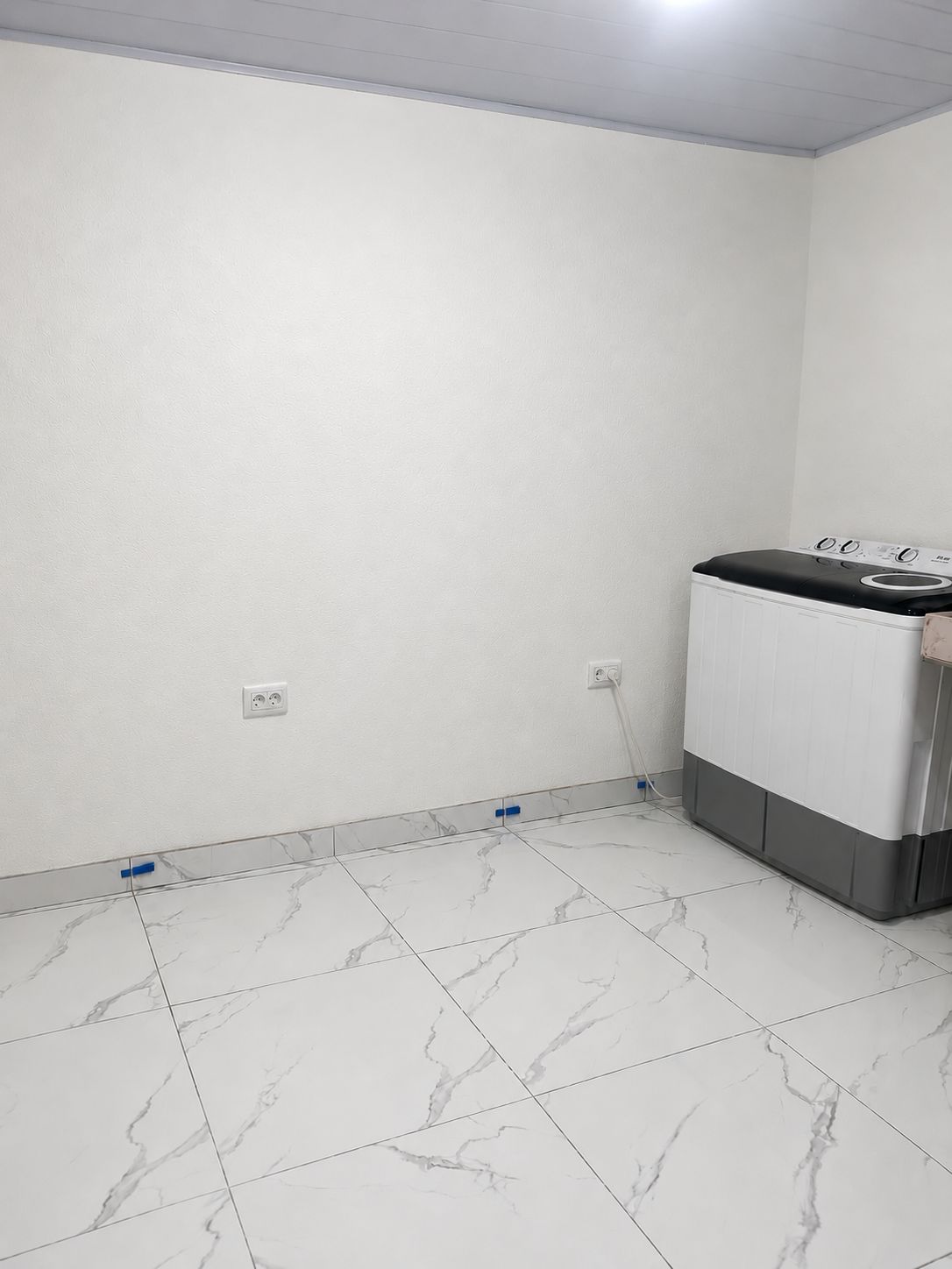 Un lavadero con lavadora, paredes blancas y baldosas de piso con diseño de mármol.