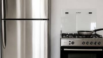 A stainless steel refrigerator and a built-in oven in a kitchen with white tiled flooring.