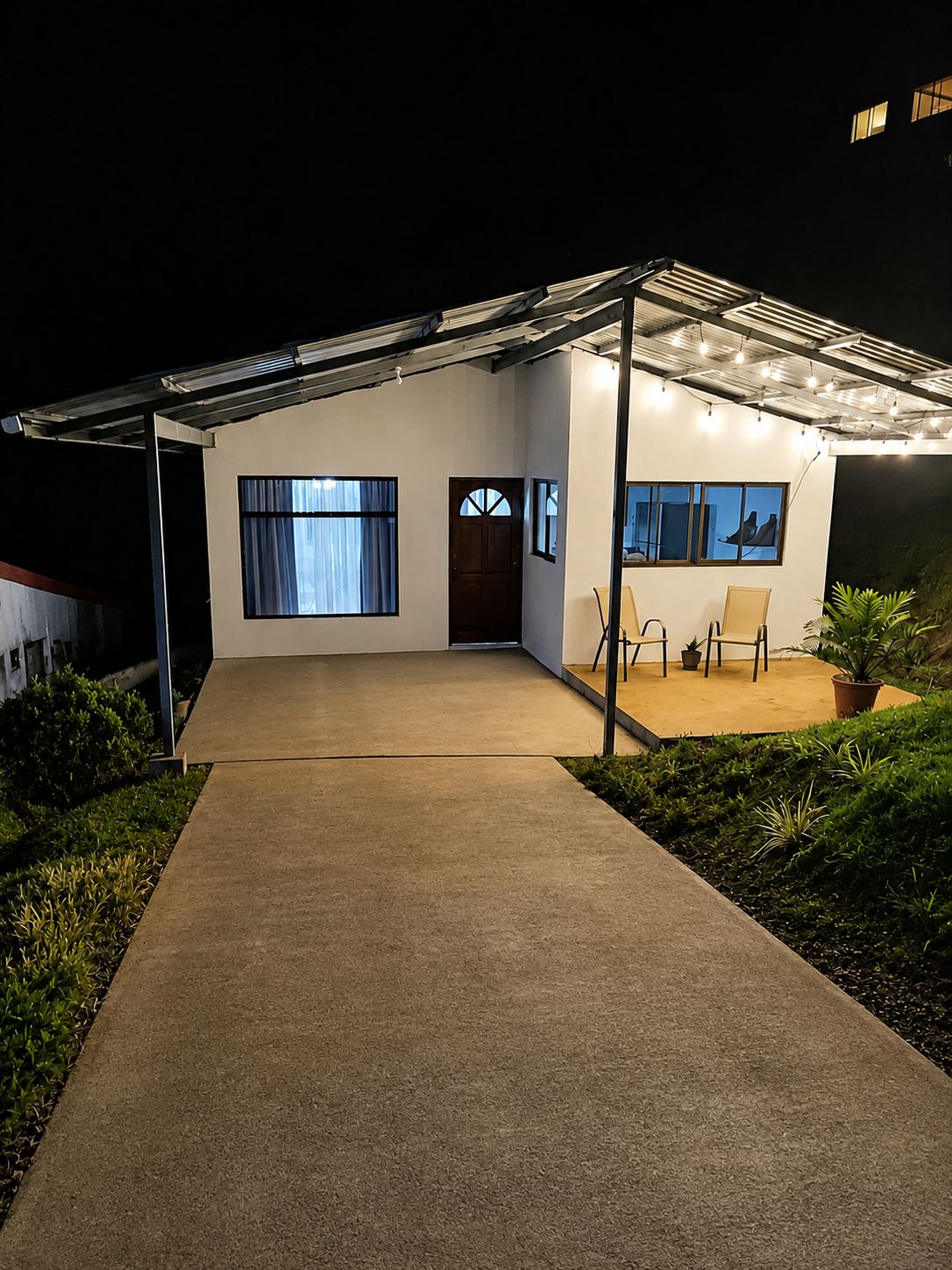 Una casa moderna con un porche cubierto, entrada de concreto y un pequeño jardín.