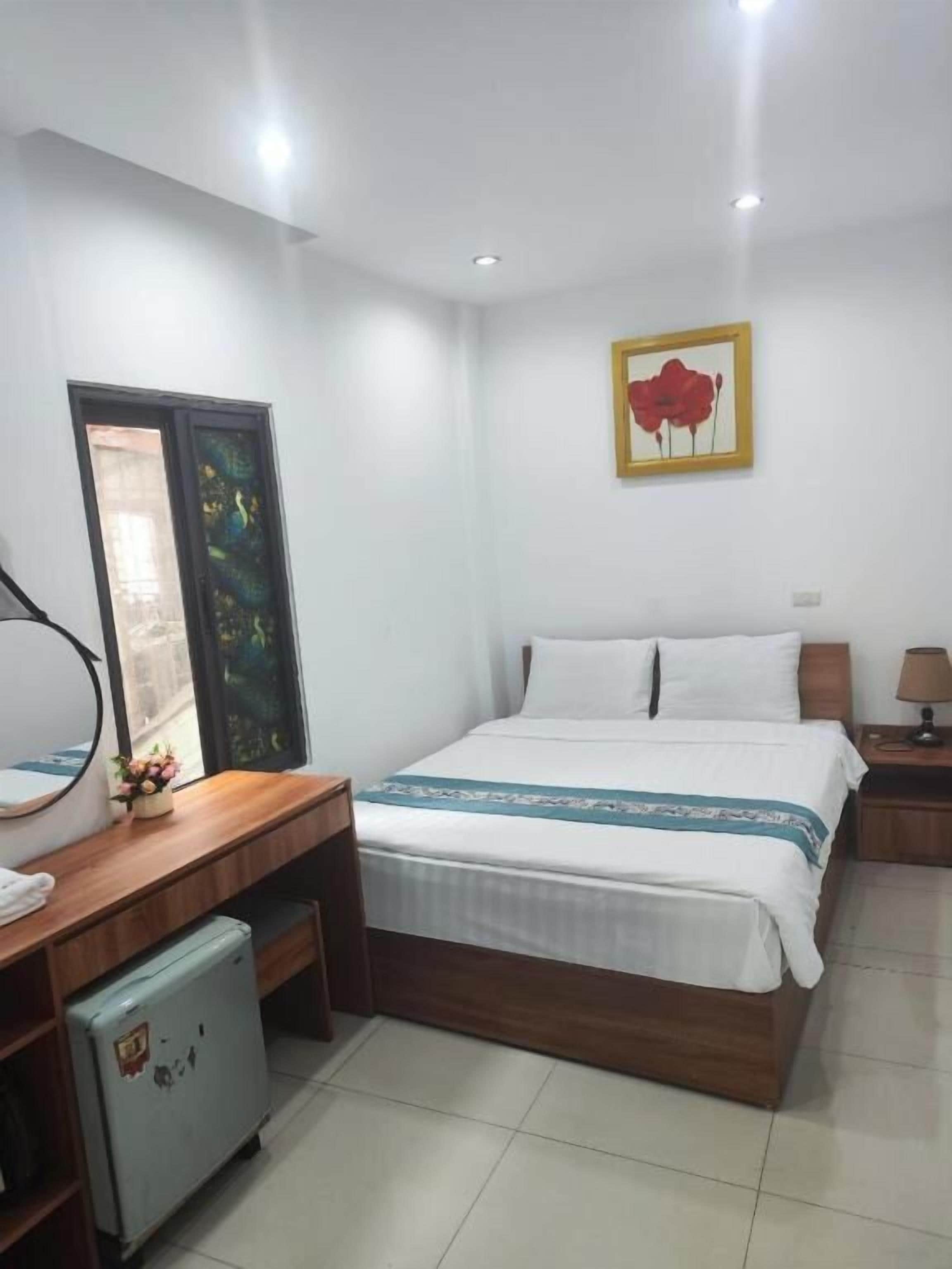 Habitación de hotel con cama, mesita de noche, lámpara y un pequeño refrigerador.
