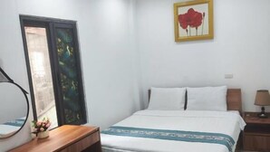 Habitación de hotel con cama, mesita de noche, lámpara y un pequeño refrigerador.