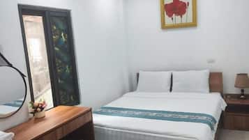 Habitación de hotel con cama, mesita de noche, lámpara y un pequeño refrigerador.