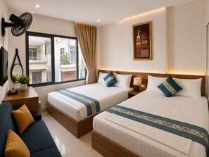 Ein Hotelzimmer mit zwei Betten, einem Sofa, einem Schreibtisch, einem Ventilator, einem Fenster mit Vorhängen und einem Wandbild.