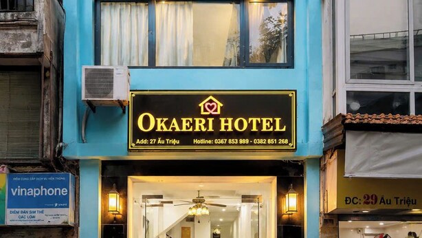 Un hotel con fachada azul, unidades de aire acondicionado, un cartel con el nombre del hotel y una entrada visible.