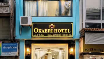 Un hotel con fachada azul, unidades de aire acondicionado, un cartel con el nombre del hotel y una entrada visible.