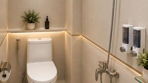 Un baño moderno con inodoro, ducha con cabezal de ducha manual y dos dispensadores de jabón en la pared.