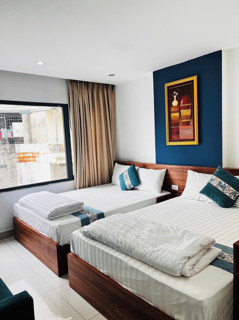A hotel room with two beds, a large window, and a framed picture on the wall.