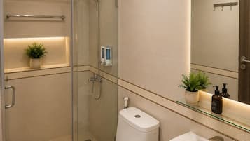 Un baño moderno con ducha envuelta en vidrio, inodoro blanco y lavamanos con espejo arriba.