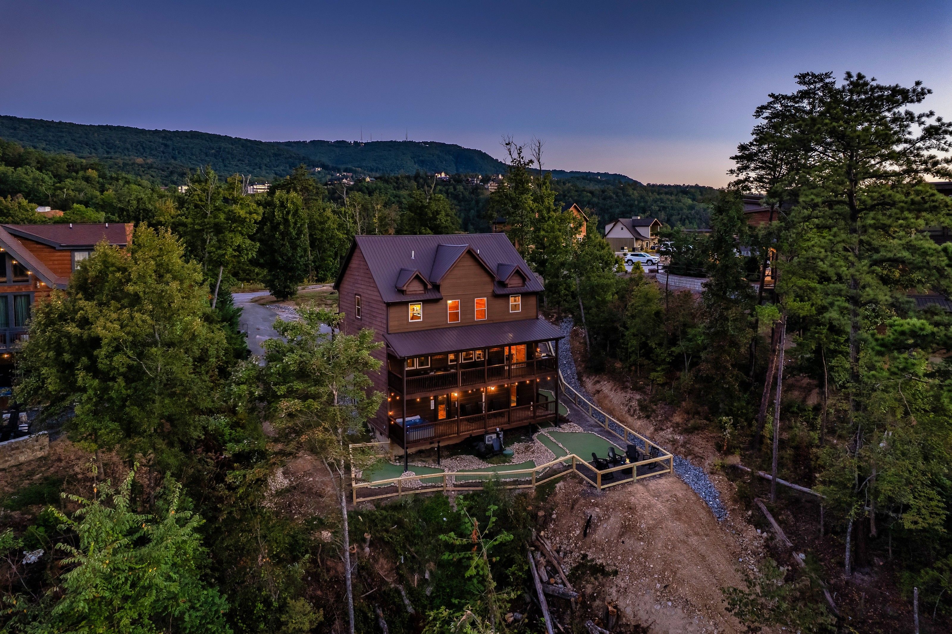 A multi-story wooden cabin with a balcony, surrounded by dense forest and a clear sky.