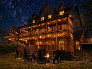 A two-story wooden cabin with multiple balconies, string lights, and outdoor seating. - Private Indoor Pool, Hot Tub, Game Room, Sleeps 12 · 20 Min to Pigeon Forge (Sevierville)