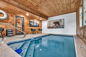 A wooden interior with a pool, a chair, a table, and a bear painting. - Heated Indoor Pool | Mtn Views | Fenced Yard | 12 (Sevierville)