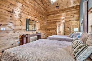 A wooden cabin-style bedroom with two beds, a dresser, a mirror, and a door. - Heated Indoor Pool | Mtn Views | Fenced Yard | 12 (Sevierville)