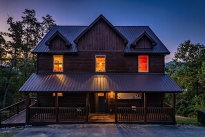 A two-story wooden house with a porch, multiple windows, and a metal roof. - Heated Indoor Pool | Mtn Views | Fenced Yard | 12 (Sevierville)