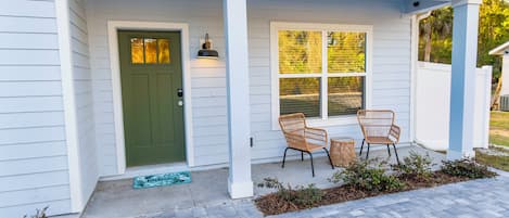 A house with a green door, a porch with two wicker chairs, and a welcome mat.