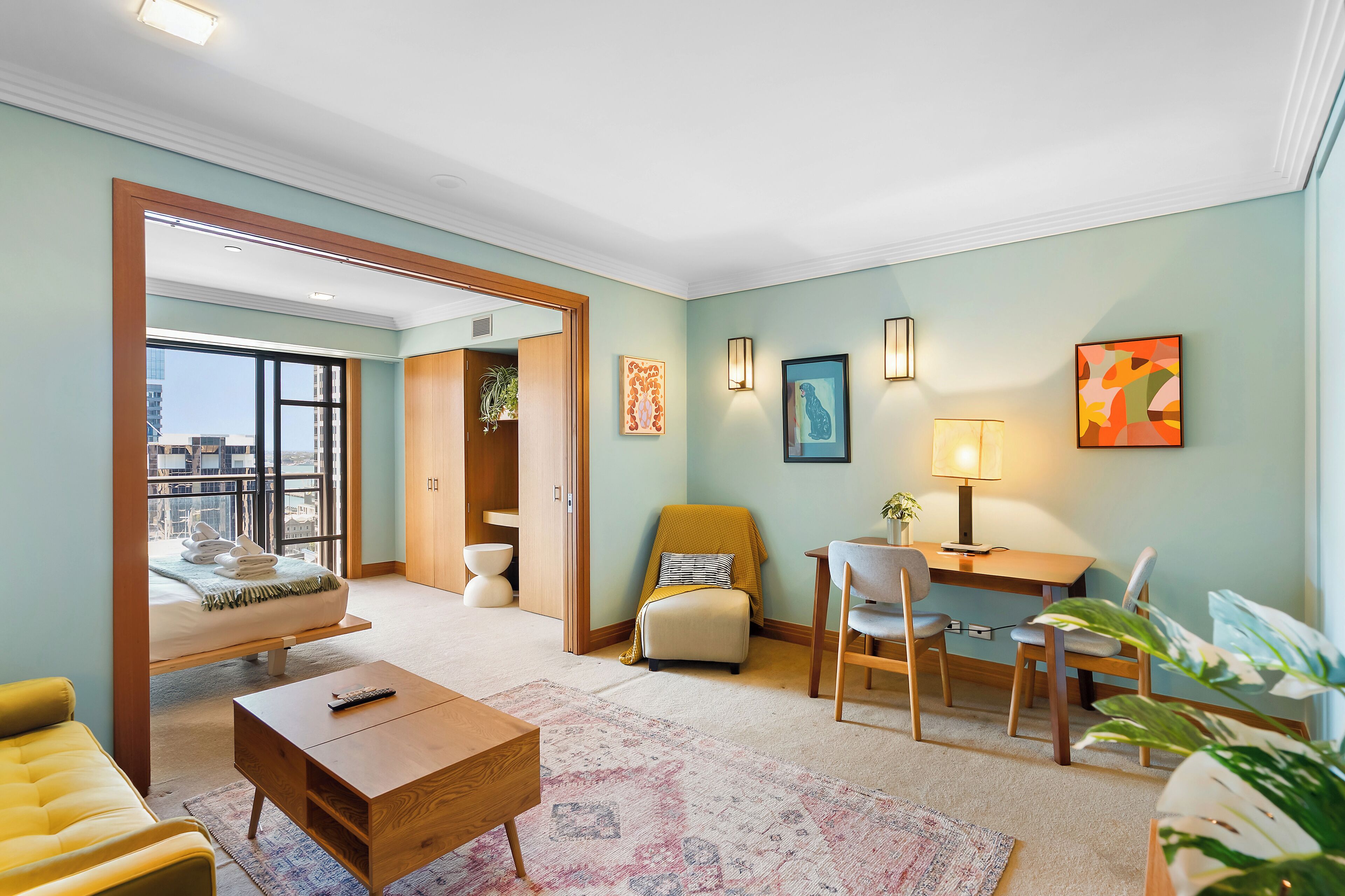 Un salon moderne comprenant un canapé, une table basse, un coin repas avec une table et des chaises, et une vue dégagée sur l’extérieur grâce à une grande fenêtre.