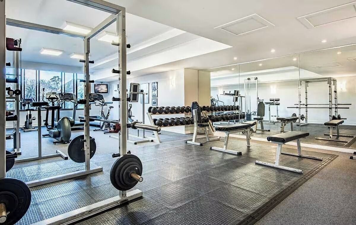Uma academia com equipamentos de musculação, aparelhos de cardio e espelhos nas paredes.