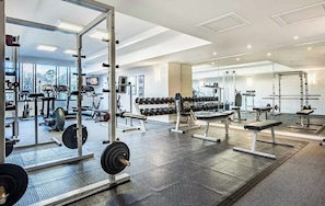 Uma academia com equipamentos de musculação, aparelhos de cardio e espelhos nas paredes.
