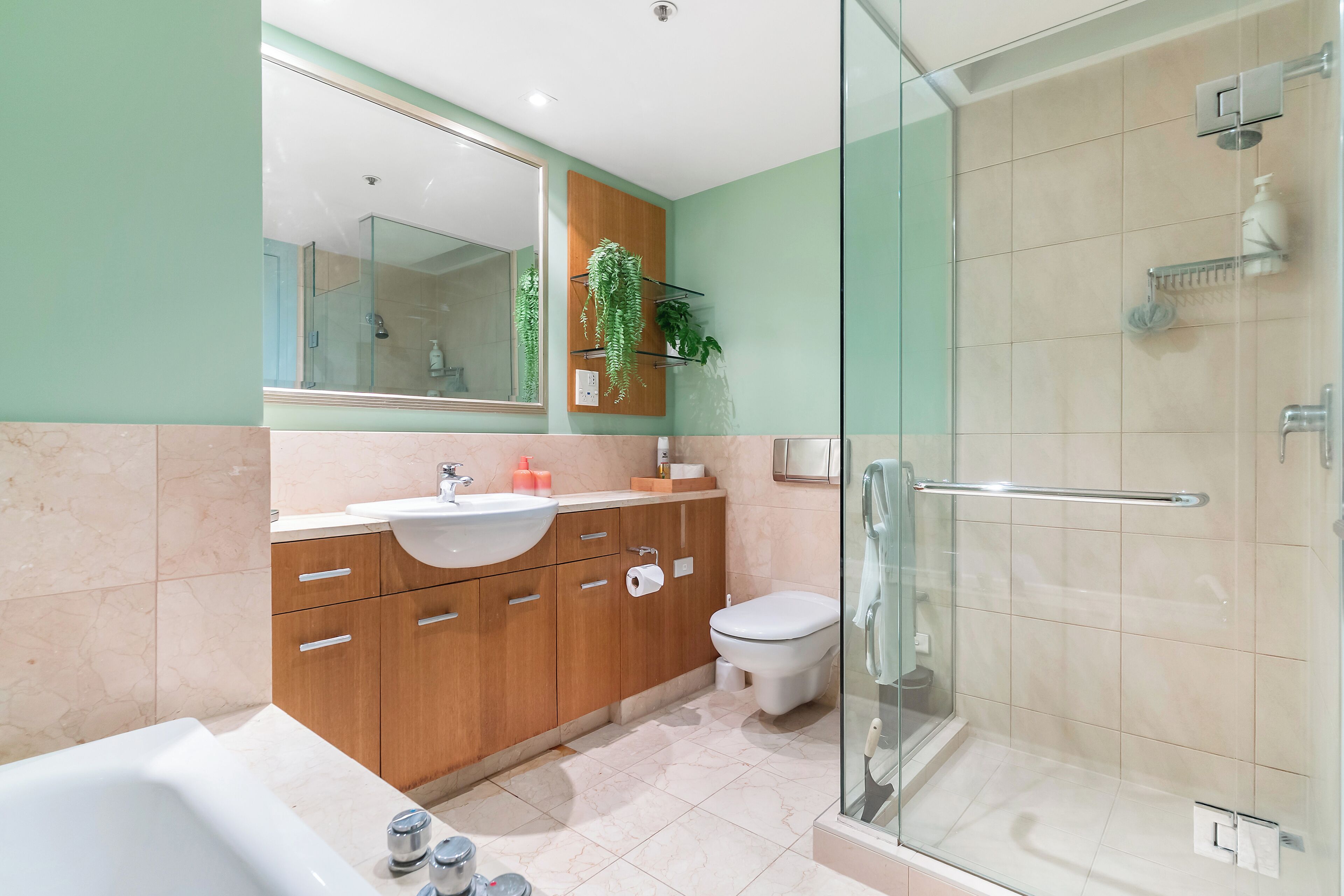 A modern bathroom with a glass shower enclosure, a sink with a marble countertop, and wooden cabinets.