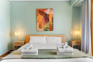 Quarto de hotel com cama, duas mesas de cabeceira, um quadro na parede e uma janela com cortinas.