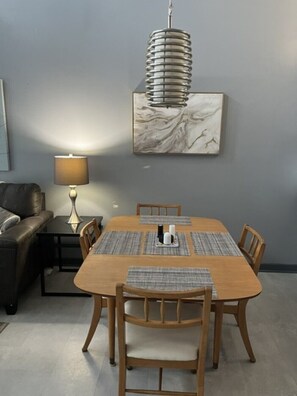 Een eetruimte met een houten tafel, zes stoelen, een centraal lichtarmatuur, een marmeren kunstwerk aan de muur en een lamp op een bijzettafeltje.