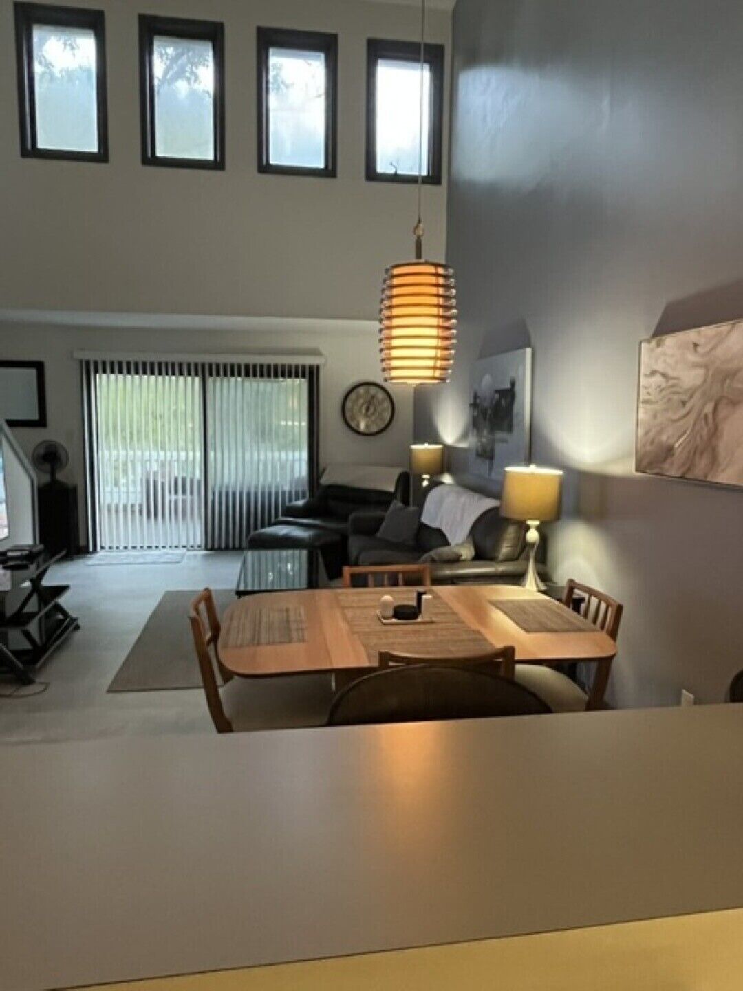 A modern living room with a dining area, large windows, and a hanging lamp.