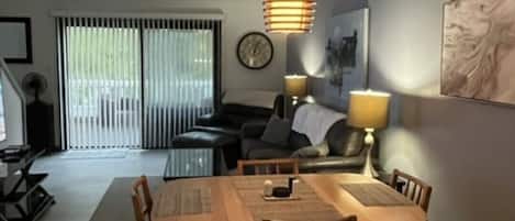 Una sala de estar moderna con comedor, ventanas amplias y una lámpara colgante.