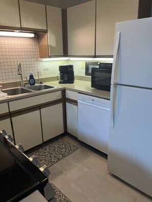 Eine kompakte Küche mit Geschirrspüler, Kühlschrank, Mikrowelle und Kaffeemaschine.