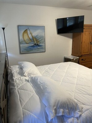 Een slaapkamer met een bed, een schilderij van een zeilboot, een televisie en een houten kast.