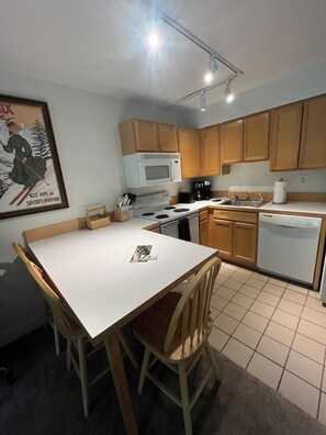A compact kitchen with wooden cabinets, a white countertop, a microwave, a stove, and a dishwasher.
