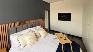 Una camera da letto moderna con un letto, una testata in legno, un tavolino con bicchieri e un quadro appeso al muro.