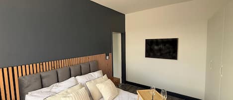 Een moderne slaapkamer met een bed, een houten hoofdbord, een klein tafeltje met glazen en een schilderij aan de muur.