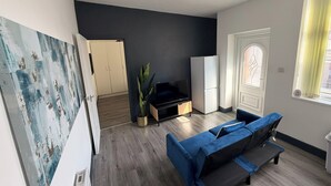 Un soggiorno con un divano blu, una TV su un supporto in legno, una pianta e un armadio.