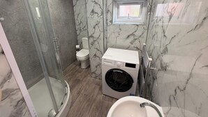 Un bagno con cabina doccia in vetro, un water, una lavatrice e un lavandino.