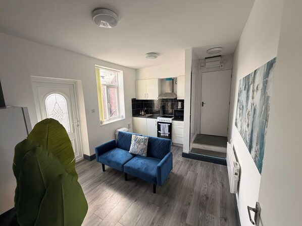 Een kleine leefruimte met een kitchenette, een bank en een deur naar een badkamer.