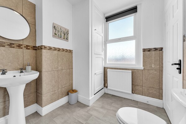 Ein Badezimmer mit einem weißen Waschbecken, einem Spiegel, einer Toilette und einem Fenster.