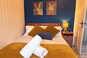 Habitación de hotel con una cama, almohadas, una mesita de noche y dos cuadros colgados en la pared.